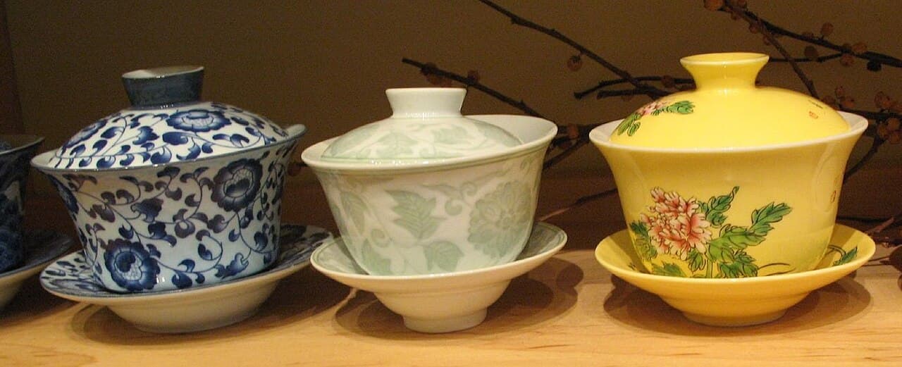 A white porcelain gaiwan and tasting cups on a tea tray